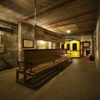 Bunkerraum mit einer Holzbank und einem Schild der U-Bahn-Station Gesundbrunnen sowie gelbem U-Bahn-Wagen